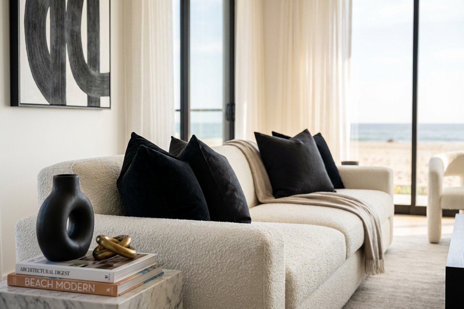 A bouclé sofa with black velvet cushions beside sheer drapery